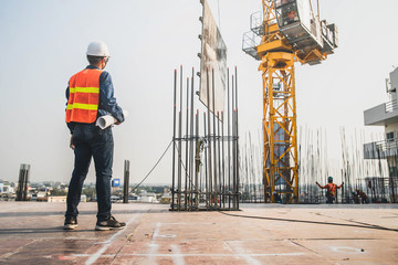 Engineer in hardhat and orange jacket posing on building site. civil engineer or architect with hardhat on construction site checking schedule on plan.