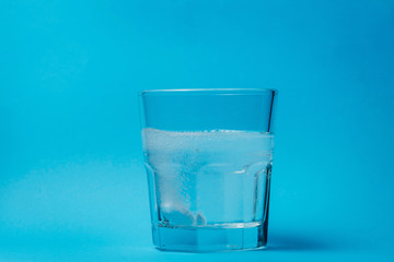 Close up of painkiller tablet in glass of water over blue background