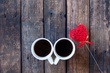Red heart on a stick and two white cups with tea or coffee. On a wooden table