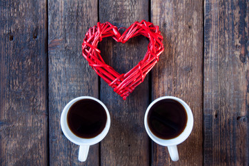 Red wicker heart and two white cups with tea or coffee. On a wooden table