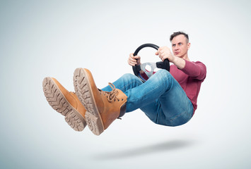 Man in jeans and red t-shirt drives a car with a steering wheel, on light background. Auto driver...