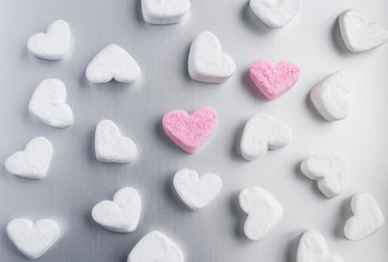 two pink marshmallow hearts lies among white sugar marshmallows in the shape of hearts evenly laid out on a gray aluminum background