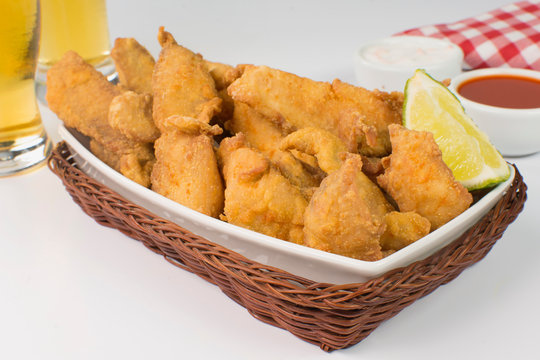 Fried Tilapia strips in platter with beer and sauces in white background