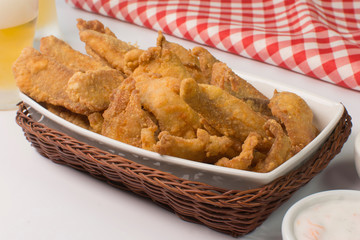 Fried Tilapia strips in platter with beer and sauces in white background with half light