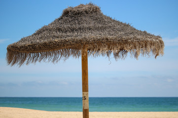 A parasol stands on an empty sunny beach in the Algarve, Portugal