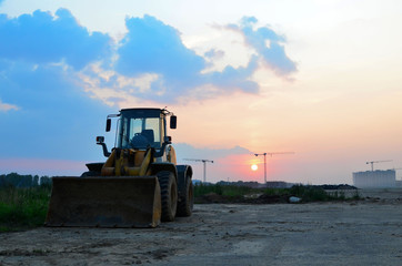 Front-end loader working on construction site during the renovation of the road. Laying or replacement of underground storm sewer pipes. Installation of water main, sanitary sewer, storm drain systems