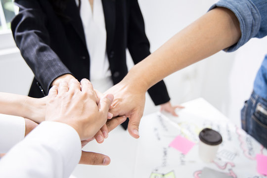Colleagues are gathering hands to encourage each other to work. For successfully complete project. Employees are working in modern office. (Agile and Scrum in retrospective and sprint review process).