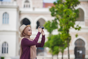 Portrait of beautiful young solo Muslim traveler taking photograph