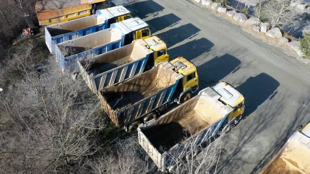 Row of a dump trucks prepared for work in open cast mine. Industry and transportation as a source of emissions. Deforestation european landscape.