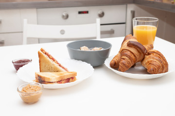 Tasty and healthy breakfast. Croissants, orange juice, a sandwich with jam and peanut butter, granola with yogurt, banana and apple