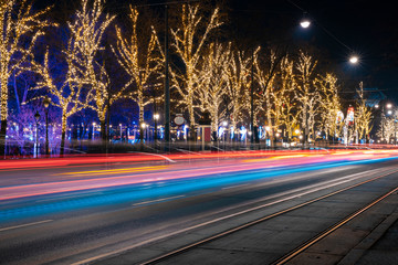 Fototapeta na wymiar long exposure night city light festive street urban view colorful illumination from fuzzy cars headlights and garlands on trees