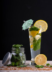 Lemon juice cocktail with ice and mint, accompanied by a glass jar with mint on a wooden base.