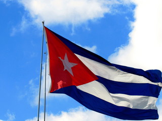 National flag of Cuba on flagpole in front of blue sky.