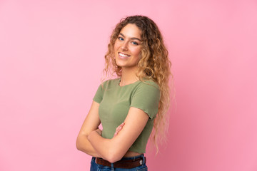 Young blonde woman with curly hair isolated on pink background with arms crossed and looking forward