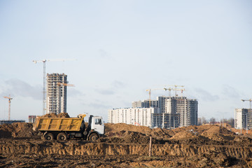 Heavy dump trucks and hydraulic luffing jib tower cranes works at a construction site. Tower crane...