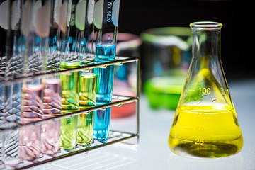 Yellow chemical liquid containing in flask with lab glassware on black background, la research and...