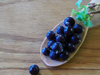 Frozen delicious black currant berries and young twigs with green leaves in a wooden spoon on a wooden background closeup. Beautiful picture of the fruit harvest for printing the cover
