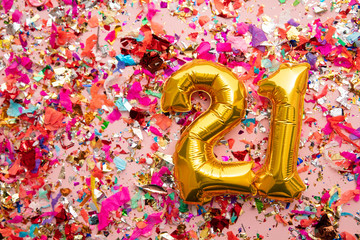 Number 21 gold birthday celebration balloon on a confetti glitter background