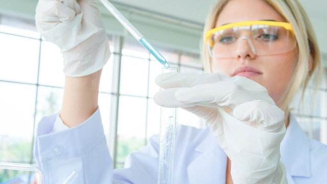 close up face of female scientist holding a tube and beaker with liquid substance. woman research is working in the Laboratory. - Powered by Adobe