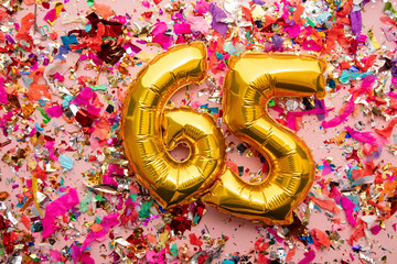 Number 65 gold birthday celebration balloon on a confetti glitter background