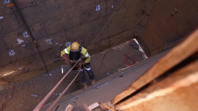 Footage of rope access industrial technician fitters, boilermaker wearing fully safety harness, helmet head welding mask eyes protection abseiling working maintenance  using oxy cutting lifting 
