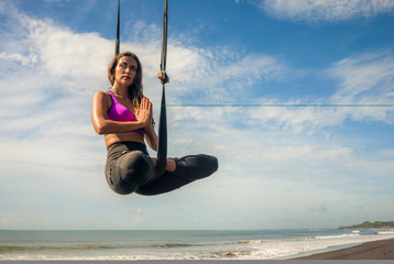 aero yoga beach workout - young attractive and athletic woman practicing aerial yoga meditation...