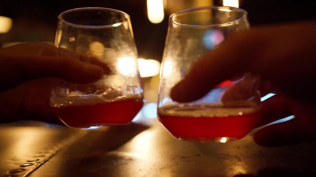 two beer glasses on table in bar. hands taking goblets, clinking, drinking and puts on the table