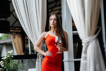 Beautiful young girl drinks wine on the veranda of a beautiful house. Holiday.