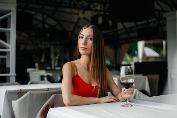 Beautiful young girl sits and drinks wine on the veranda of a beautiful house. Holiday.