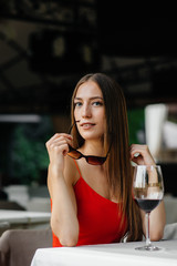 Beautiful young girl sits and drinks wine on the veranda of a beautiful house. Holiday.