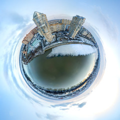 a pair of typical high-rise apartment buildings built in 2010 are on the snowy Christmas embankment of the Kuban River. Minor planet air drone view winter landscape over dark water and snowy beach nea
