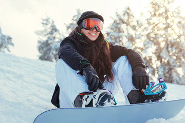 Stock photo of a young woman snowboarder sitting on the snow and smiling