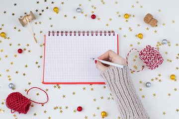 Festive background: a notebook and the hand of a woman in a sweater writes with a pen, confetti, gold stars, ribbons, a cork from champagne