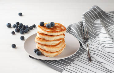 Russian traditional cuisine, wheat flour pancakes on a light plate on a white table, pancakes with berries, blueberries on the table