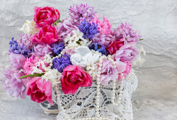 in a wicker basket a bouquet of hyacinths and tulips, lace doily, pearl beads and angel figurine