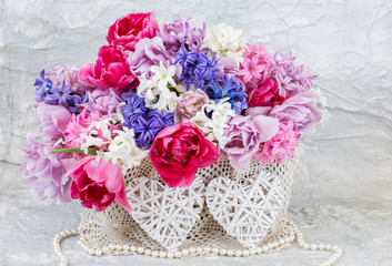 in a wicker basket a bouquet of hyacinths and tulips, pearl beads and two wicker hearts