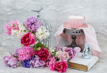 decorative cell and flowers in it: hyacinths and tulips, a tea cup, a book and an angel figurine