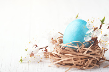 Obraz na płótnie Canvas Nest with blue egg decorated blossoming branches on white wooden background. Easter concept.