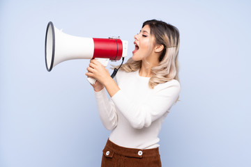 Young teenager girl over isolated blue background shouting through a megaphone