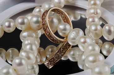 Gold ring with diamonds lies with pearl beads on the mirror
