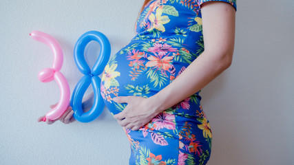 A close up photo of a pregnant young woman holding in her hands the week number thirty eight (38)...