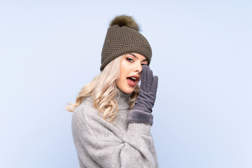 Young teenager girl with winter hat over isolated blue background whispering something