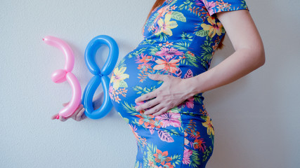 A close up photo of a pregnant young woman holding in her hands the week number thirty eight (38)...