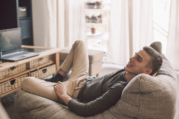 Handsome teenage guy relaxing on modern soft couch at home in living room