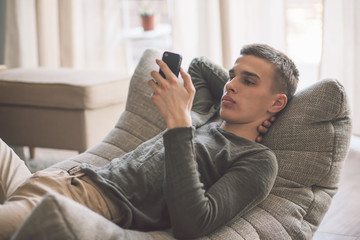 Handsome teenage guy relaxing on modern soft couch at home in living room