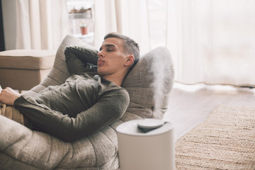 Handsome teenage guy relaxing on modern soft couch at home in living room