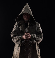 monk in a hood with a sword on a black background