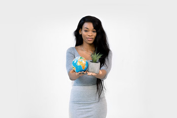 Beautiful smiling African woman showing planet earth globe and succulent in a pot in hands, focus on woman face. Earth day, international, nature and environment protection concept