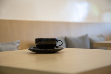 A black cup of coffee placed on a wooden table by the window in a coffee shop, Concept: Delicious breakfast drinks fragrant suitable for lifestyle, closeup cup of coffee over the top with space