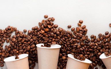Roasted coffee beans and paper cups on a gray background, top view, flat lay, free space for text....